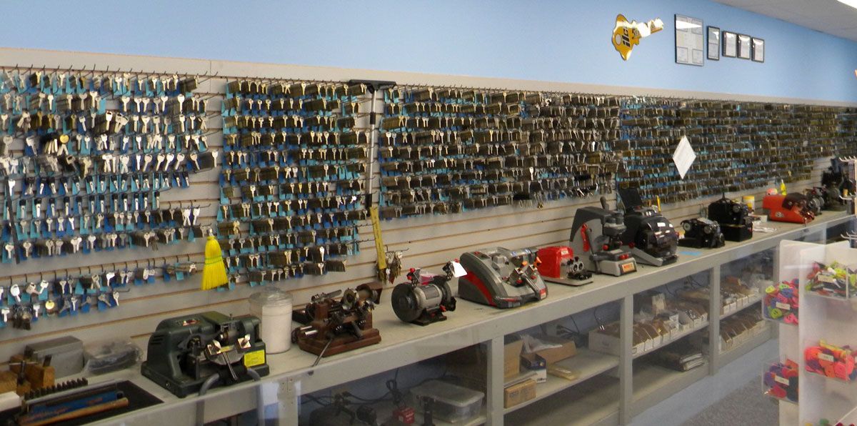 Charm's Locksmith wall display filled with hundreds of key blanks above a counter lined with key-cutting machines and locksmith tools inside a workshop.
