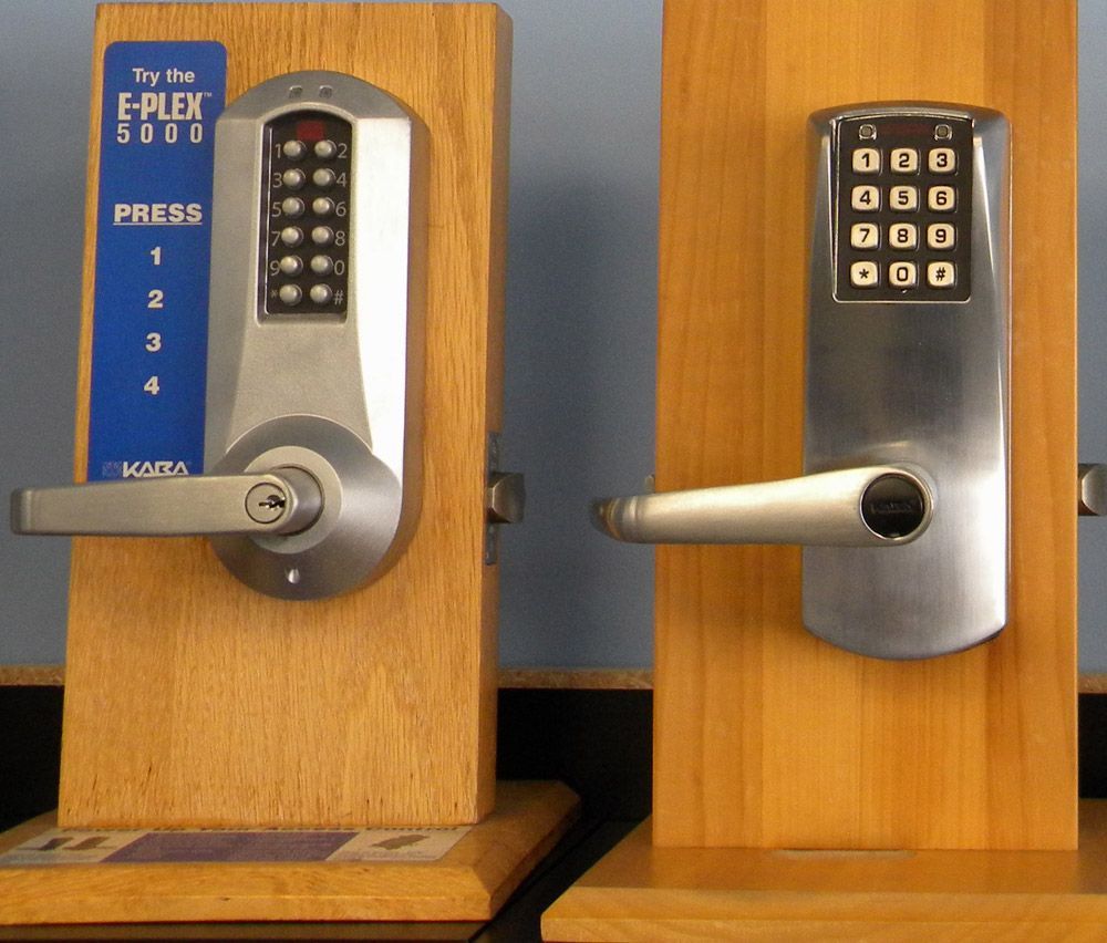 Two keypad door locks with lever handles displayed on wooden stands, showing different keypad layouts and stainless finishes.