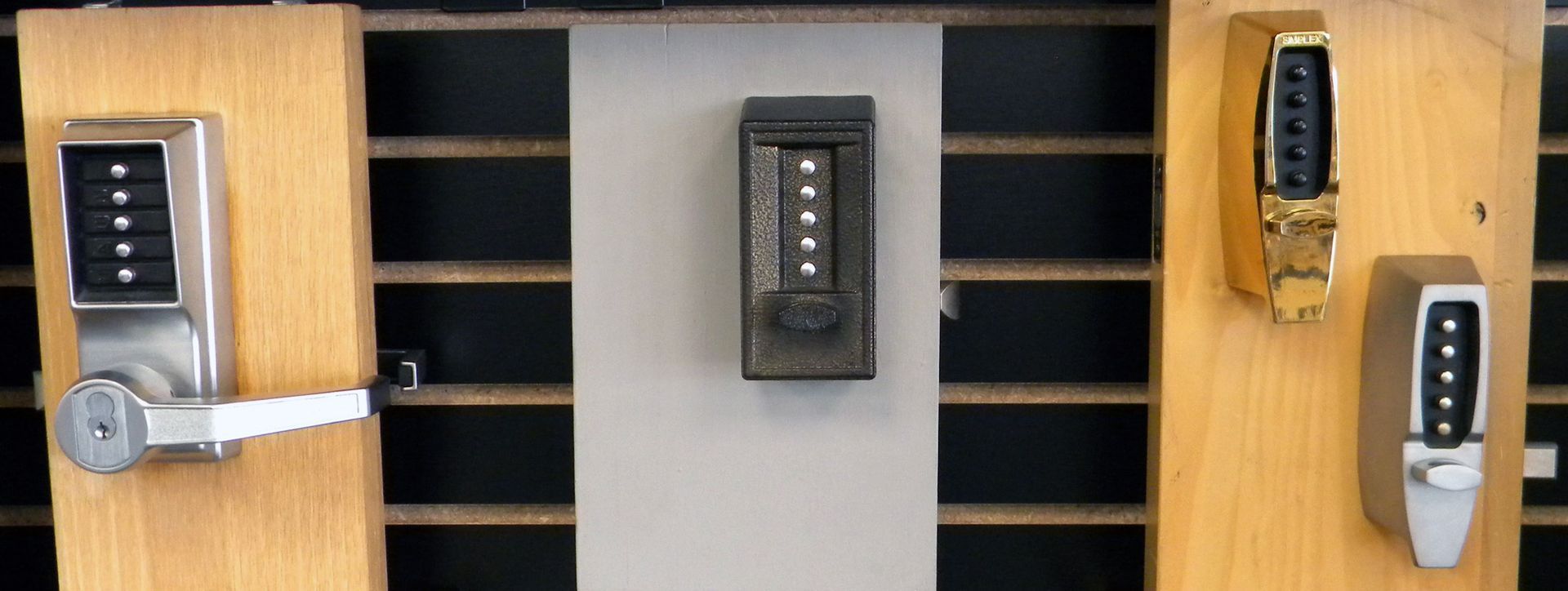 Mechanical push-button door locks in different finishes displayed on wooden mounting blocks against a slatwall background.