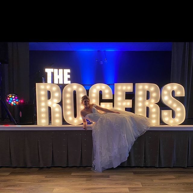 Bride in wedding dress leaning against large illuminated letters spelling
