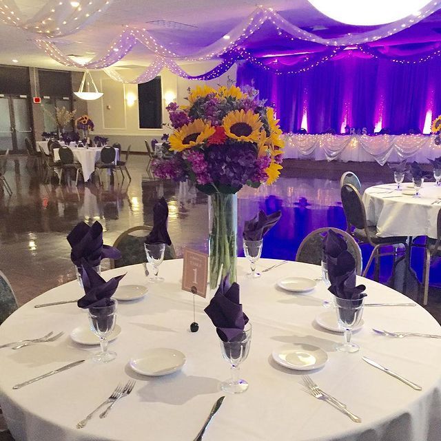 Round table set for a formal event with large sunflower and hydrangea centerpiece. Purple and white decor.