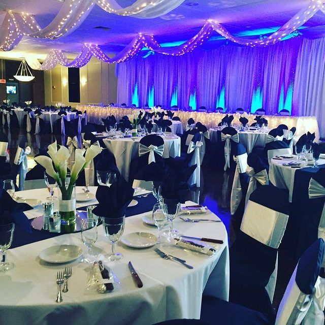 Elegant reception hall with white tables, navy accents, and blue uplighting.