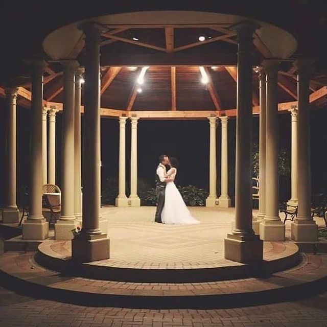Couple embracing in a gazebo at night; wedding setting with lights.