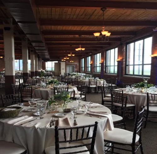 Reception hall with round tables set for a meal, under exposed beams and windows.