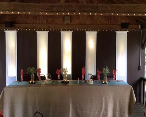 Banquet table with white fabric panels, brown wall, and string lights.