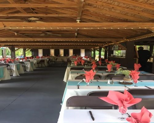 Reception hall set for a party, with tables, teal runners, coral napkins, and overhead string lights.