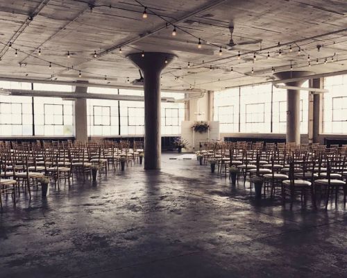 Indoor event space with rows of chairs facing a floral arrangement in front of a window.