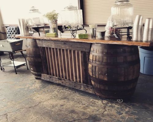 Rustic bar constructed with wooden barrels, holding beverage dispensers and cups.