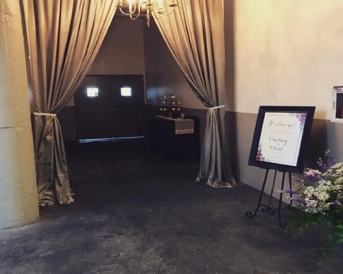 Entrance with gray curtains, a welcome sign, and floral arrangements.
