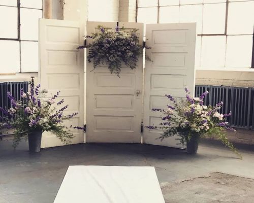 White doors decorated with floral arrangements for a wedding ceremony.