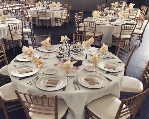 Wedding reception tables set with white linens, beige napkins, and silver chargers.