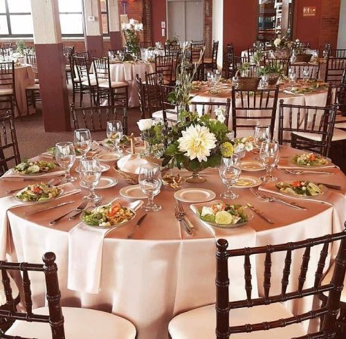 Round tables set for a formal event with centerpieces, place settings, and brown chairs.