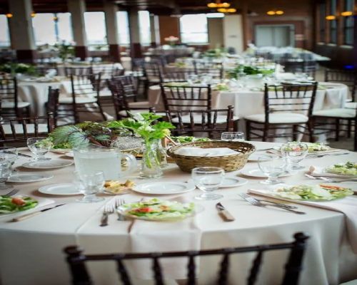 Elegant reception tables set for a wedding; neutral linens, brown chairs, floral centerpieces.