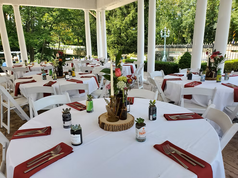 Round tables set for a gathering under a white gazebo. Red napkins and centerpieces adorn the tables.