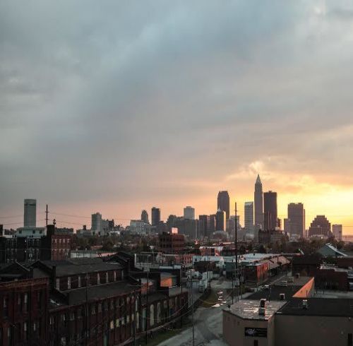 Skyline of a city at sunset with gray and orange hues; buildings in foreground.