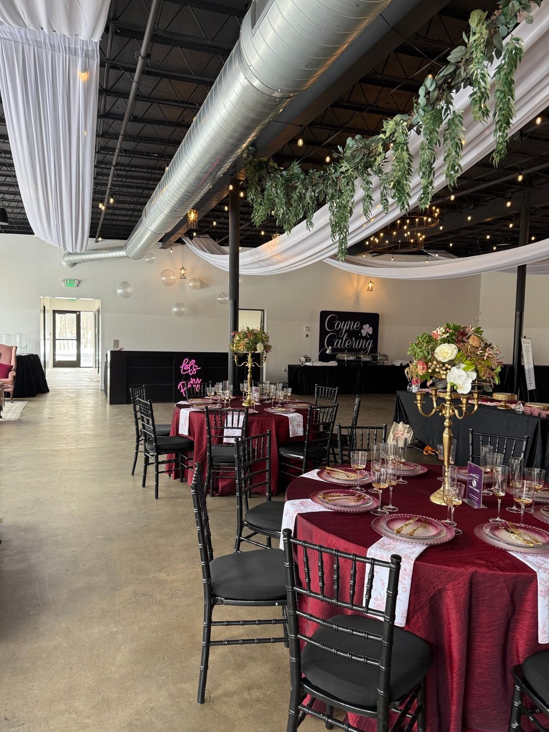Wedding reception hall with decorated tables, black chairs, and white draping.