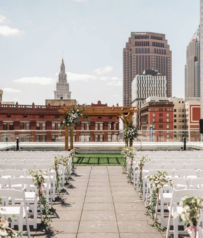 Rooftop wedding ceremony setup with city skyline backdrop, white chairs, and floral decorations.