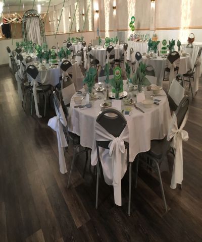Round tables set for a party, decorated with green and white accents, in a banquet hall.