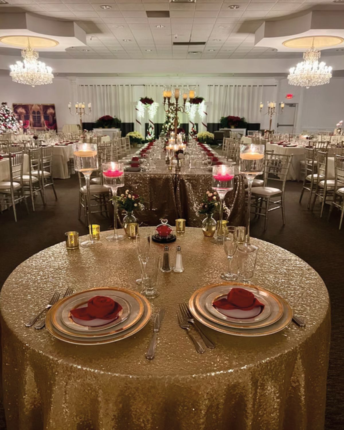 Elegant wedding reception table setting, gold sequin tablecloth, place settings with red napkins, floral centerpieces.