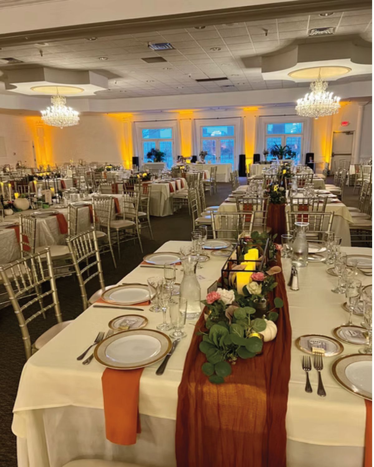 Elegant reception hall with tables set for a formal event. Orange and gold color scheme.
