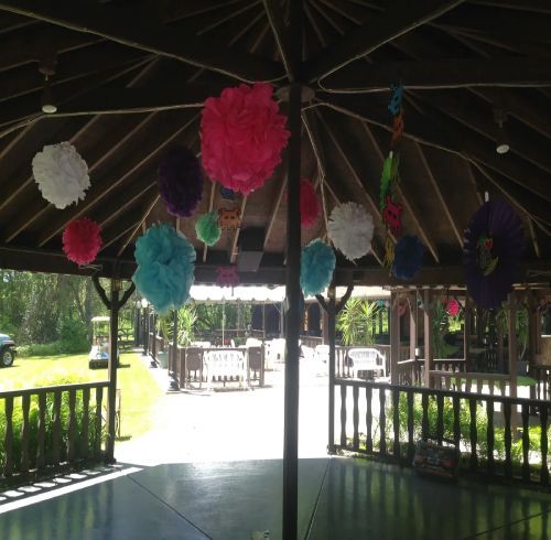 Gazebo decorated with colorful paper pom-poms; view of outdoor party area with golf cart in background.