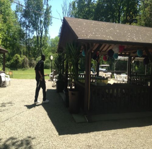 Man in dark clothes standing near a gazebo with potted plants, tables, and decorations outside.