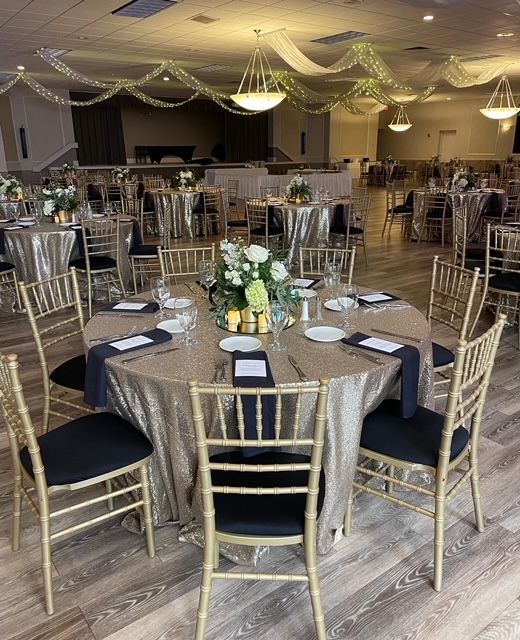 Formal event hall with round tables covered in gold sequins, black chairs, and floral centerpieces.