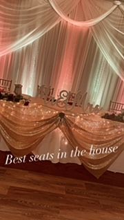 Wedding reception table with gold and white draped fabric, illuminated by warm lighting.