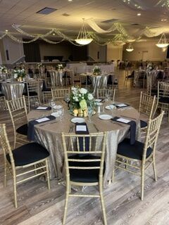 Banquet hall with round tables set for a formal event; gold chairs and sequined tablecloths.