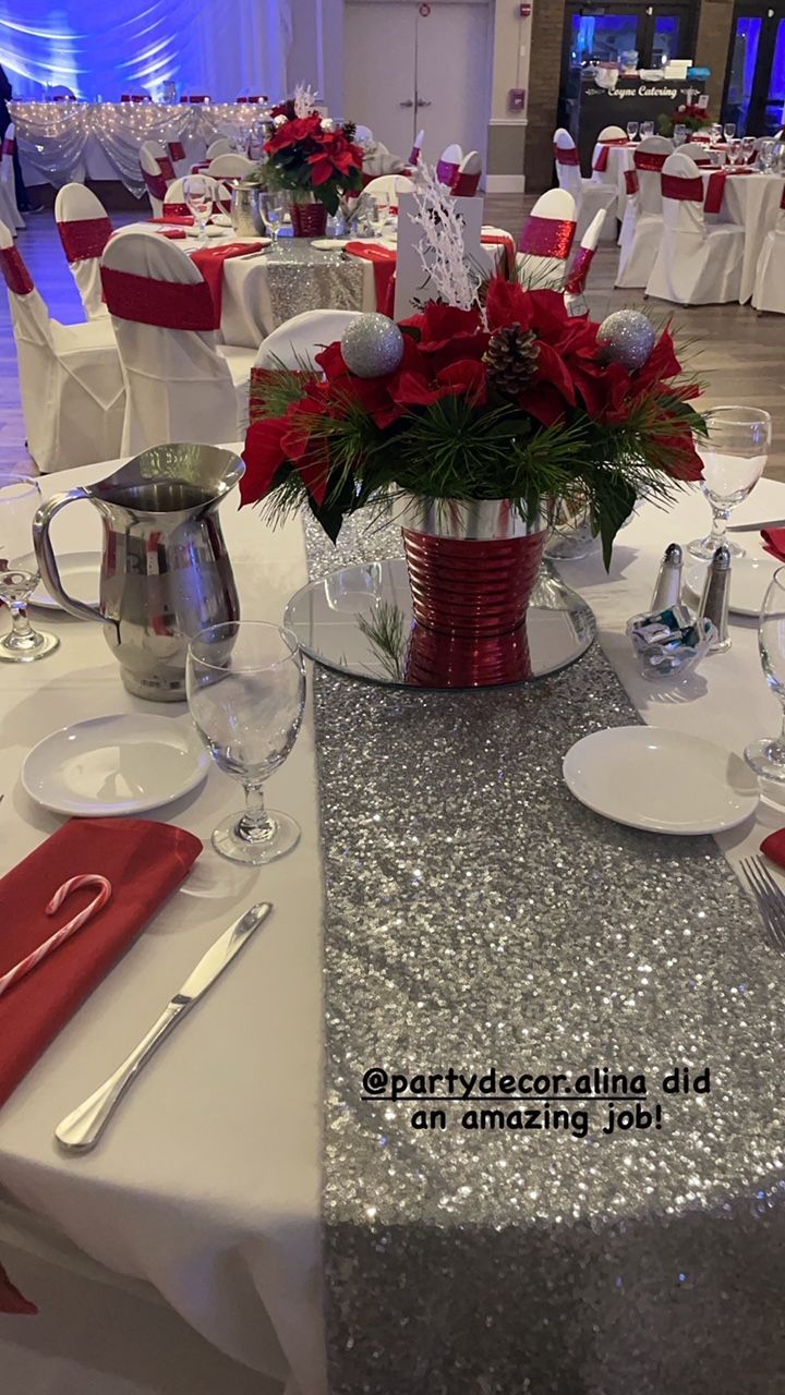 Festive table setting with red poinsettias, silver runner, and white tablecloths in a banquet hall.