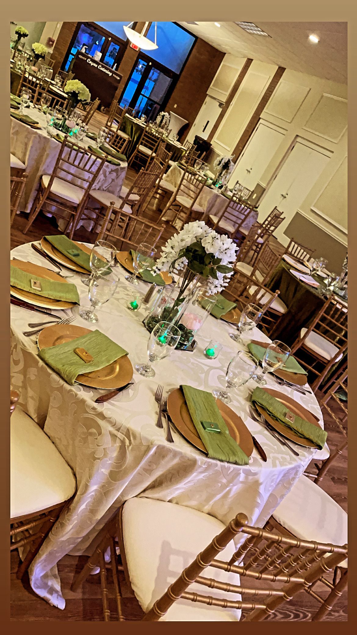 Round tables set for a formal event, featuring gold chargers, green napkins, and floral centerpieces.