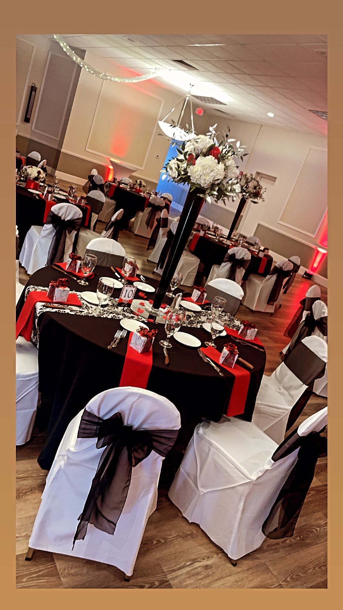 Formal event tables set with black, red, and white decor; white chair covers with black bows.
