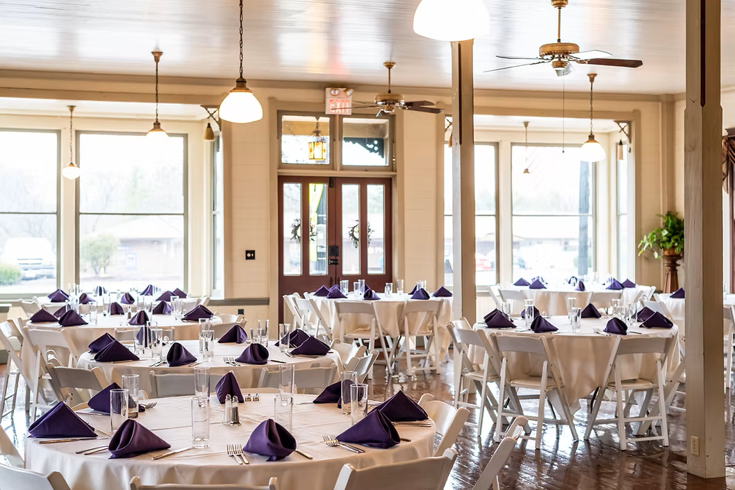 Interior view of a banquet hall, white tables with purple napkins, set for a formal event.