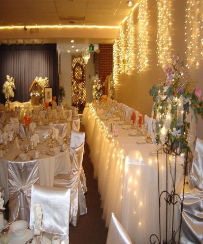 Formal dining room decorated for an event, with white linens, chairs, and fairy lights.