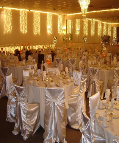 Banquet hall with round tables set for a formal event. White satin chair covers and warm lighting.