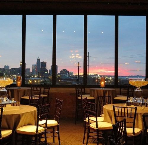 Interior view of a dining area with round tables set for a meal, a cityscape view through large windows.