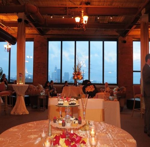 Elegant event space with city view, tables, cake stand, and people in the background.