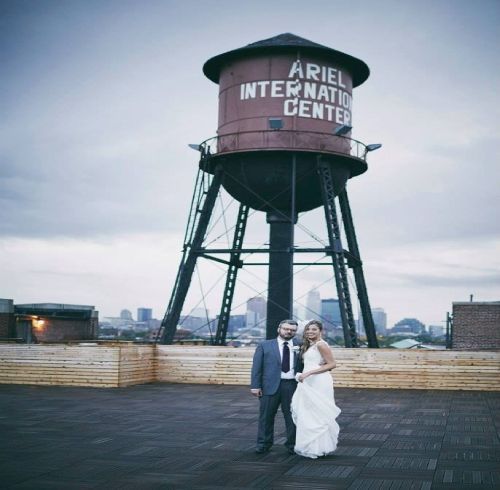 Couple in wedding attire posing on rooftop with Ariel International Center water tower, city skyline in background.