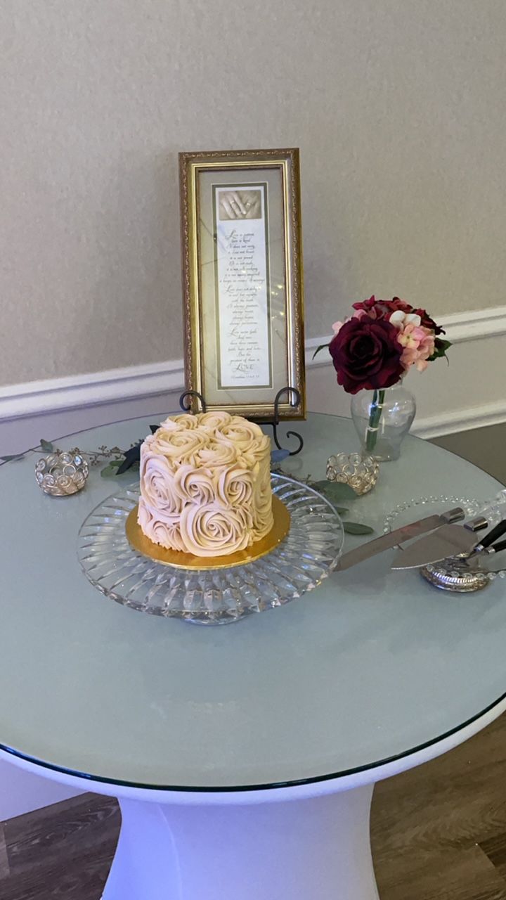 A small cake decorated with frosting rosettes on a table with flowers and framed document.