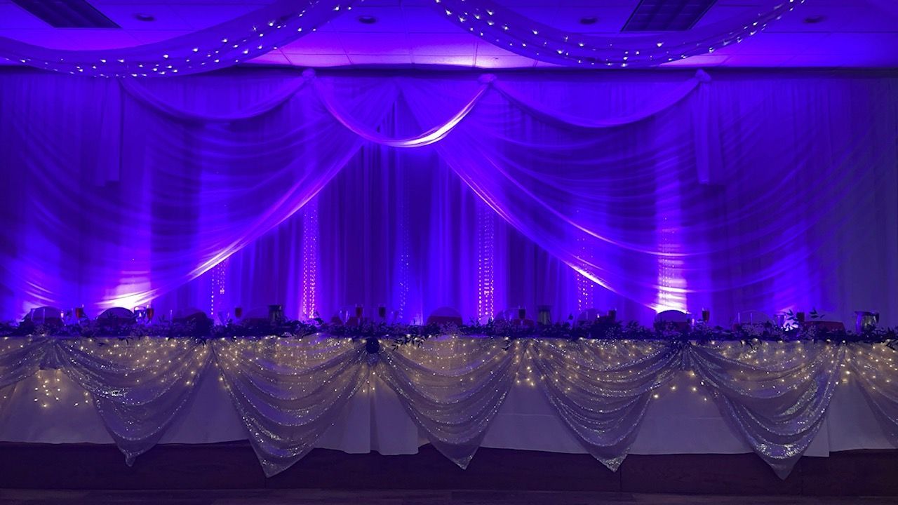 Purple-lit stage with draped fabric and fairy lights, likely for an event or celebration.