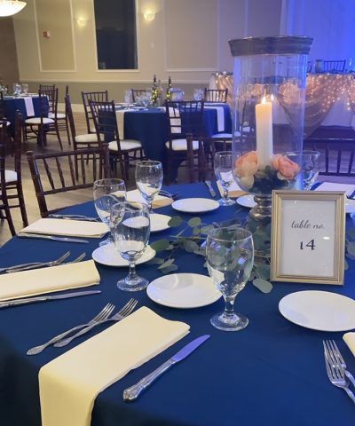 Wedding reception table set with blue tablecloth, floral centerpiece, and table number.