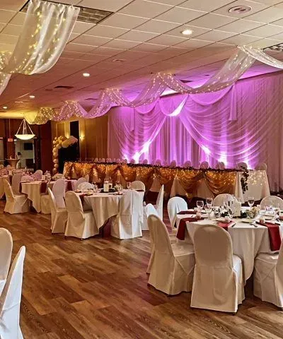 Banquet hall set for an event with round tables, white chairs, and decorative draping.