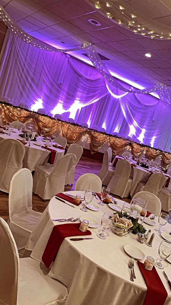 Banquet hall set for an event with round tables, white linens, red runners, and purple uplighting.