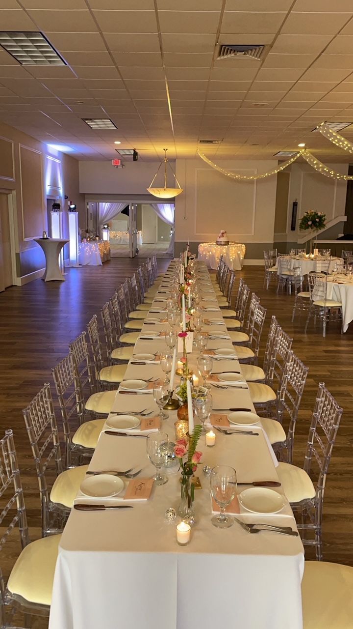 Long banquet table set for a formal event, with clear chairs and floral centerpieces.