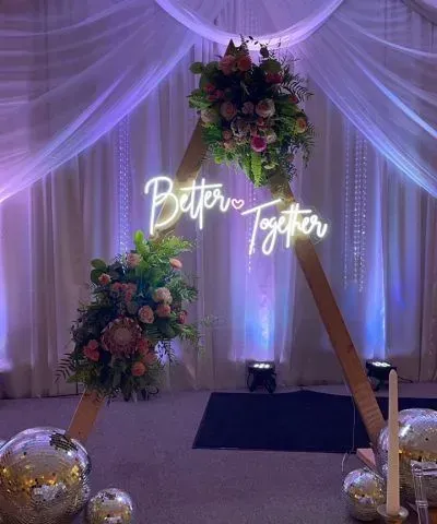 Wooden arch decorated with flowers and a neon sign reading 
