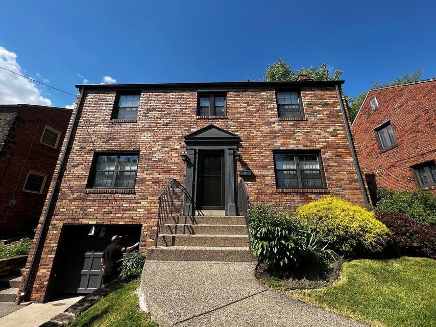 Brick apartment building with central stairway, black doors and windows, and a small shrub under a blue sky