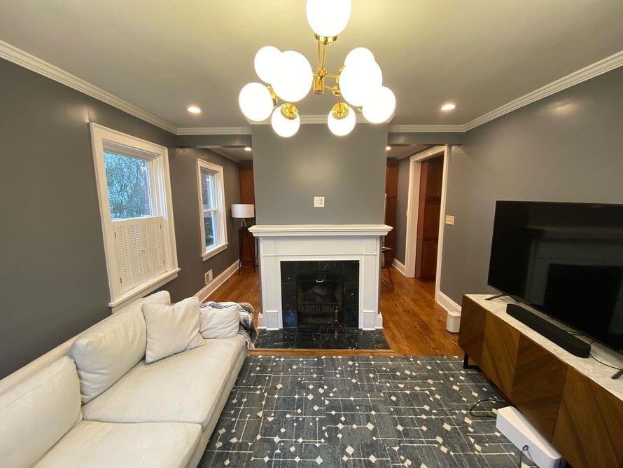 Modern living room with gray walls, white fireplace, beige sofa, patterned rug, and large TV on wood console