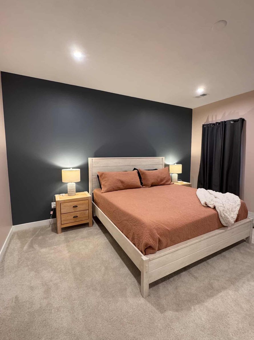 Modern bedroom with a dark accent wall, white bed, tan bedding, and bedside lamps