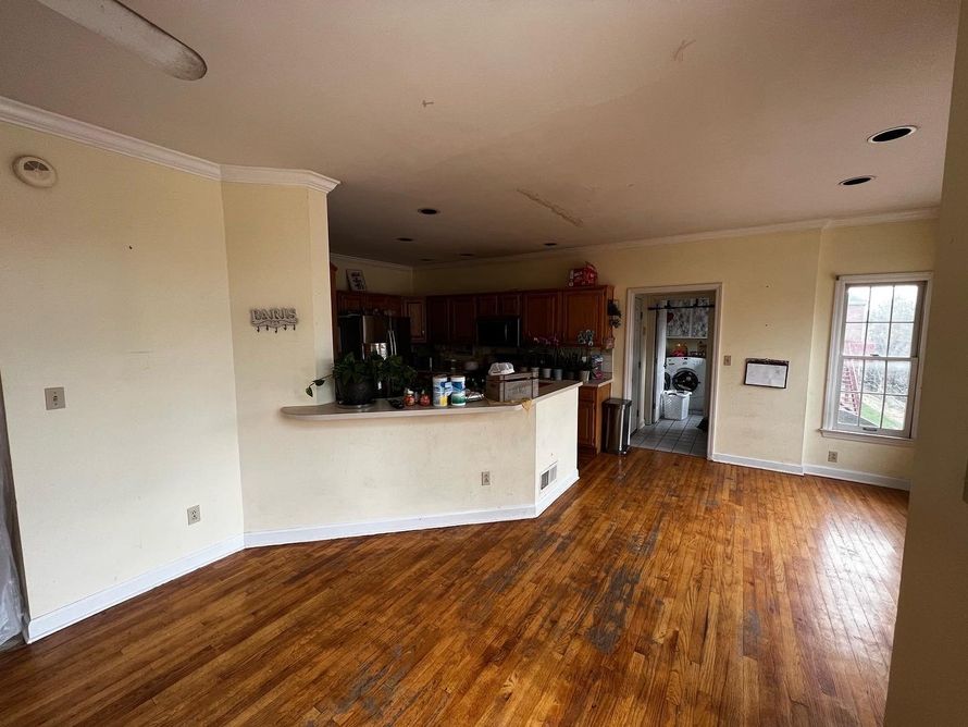 Empty living room with wood floors, white walls, and an open kitchen counter