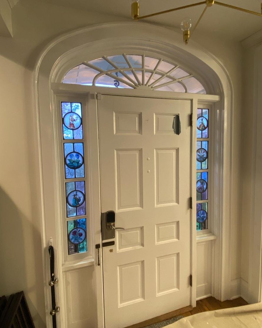 White front door with arched transom and stained-glass sidelights in a hallway
